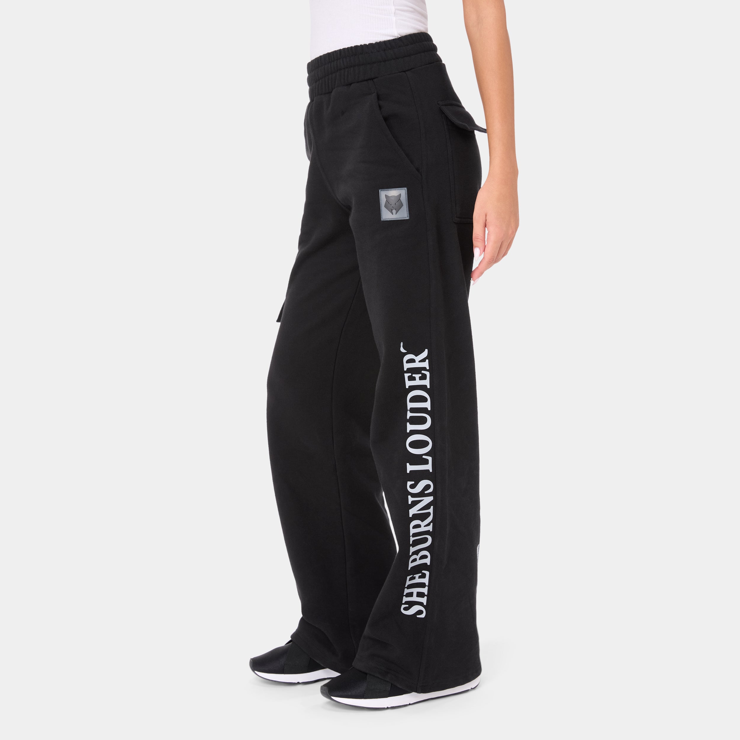 ALPHAFIRE BOTTOM — WAR BLACK — Side view waist-down, black cargo sweatpants with SHE BURNS LOUDER outlined text and