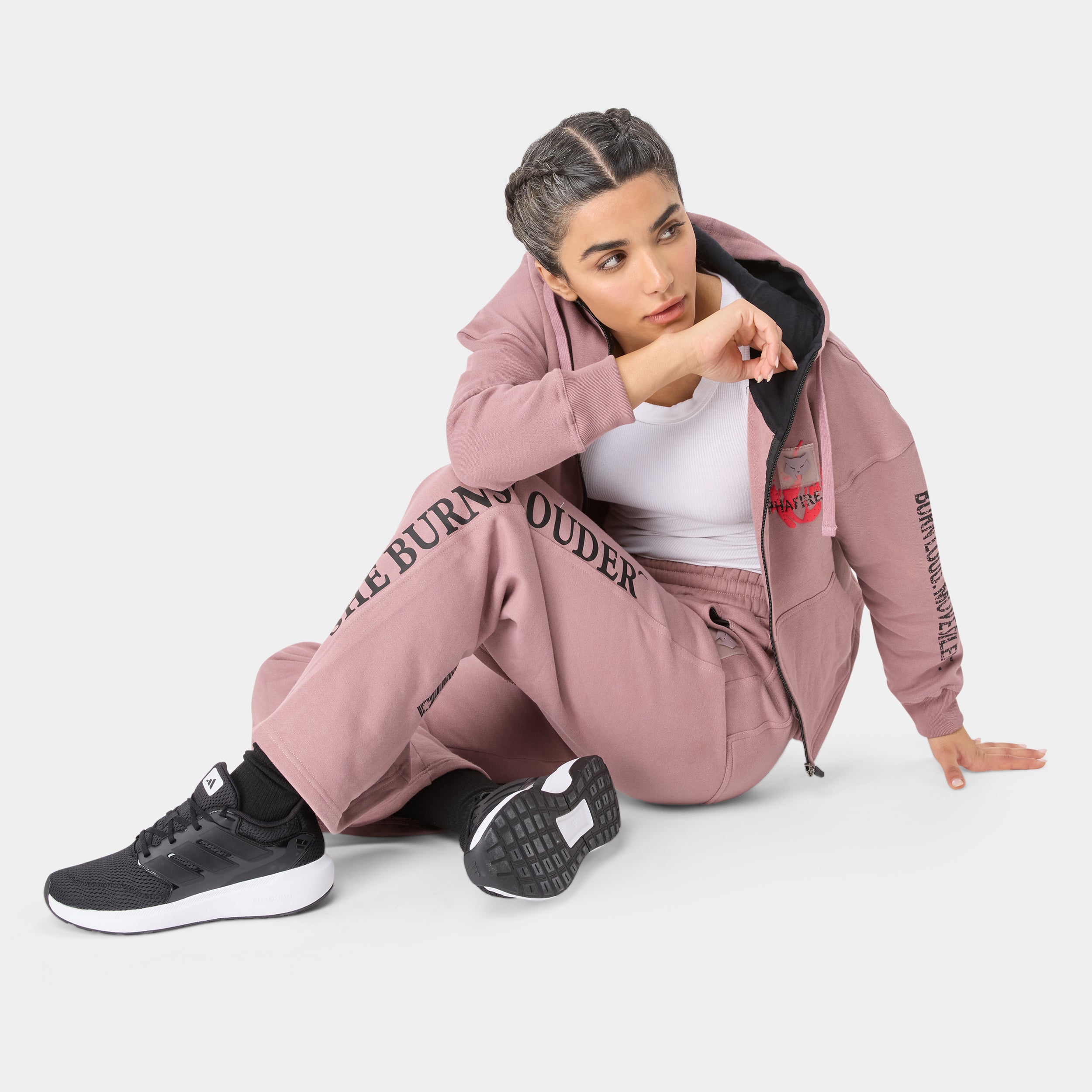ALPHAFIRE BOTTOM — STORM ROSE — Seated floor pose, full pink hoodie + pants ensemble with SHE BURNS LOUDER text and
