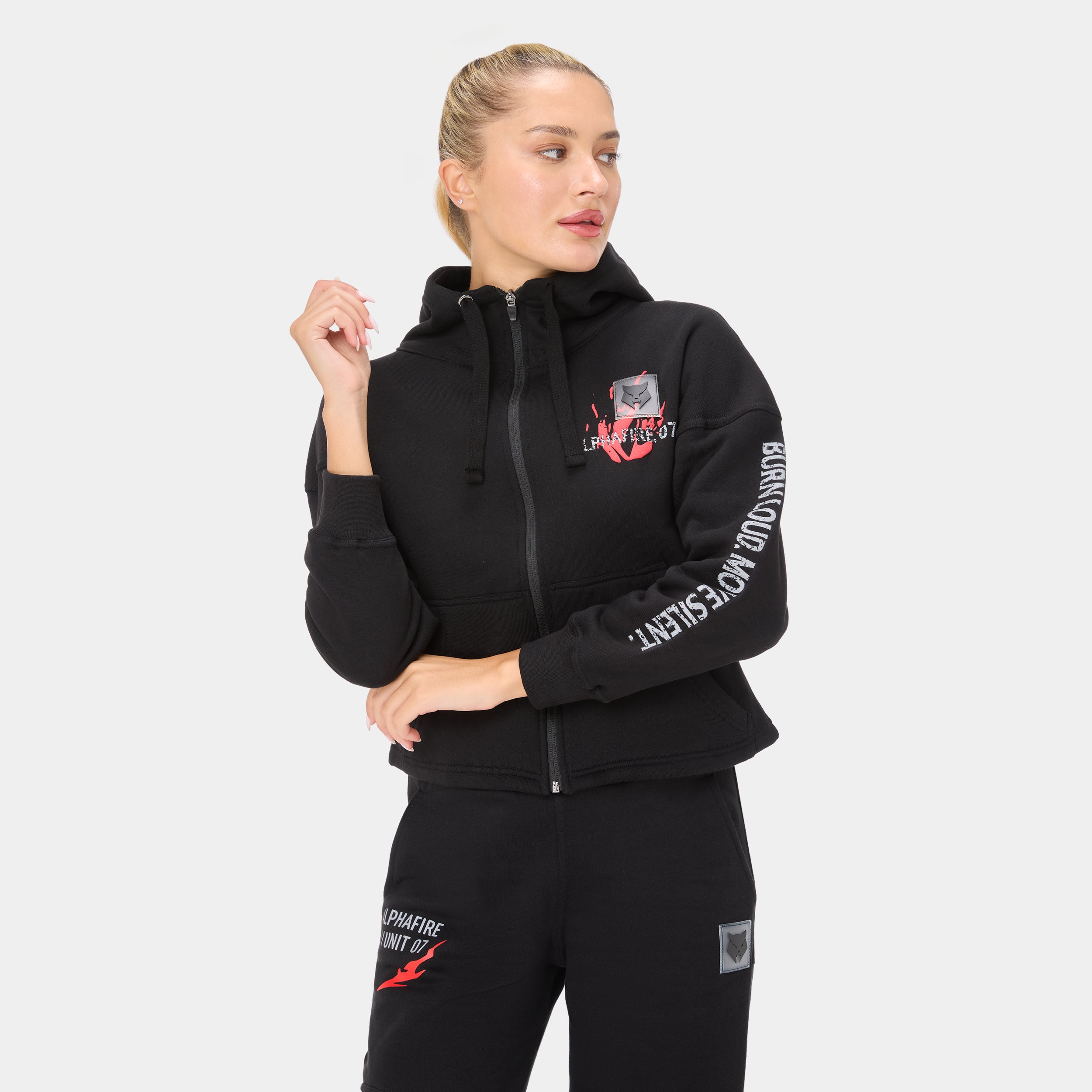 ALPHAFIRE CROP HOODIE — WAR BLACK — Front ¾ close-up, black zip hoodie with model looking right, chest logo and white