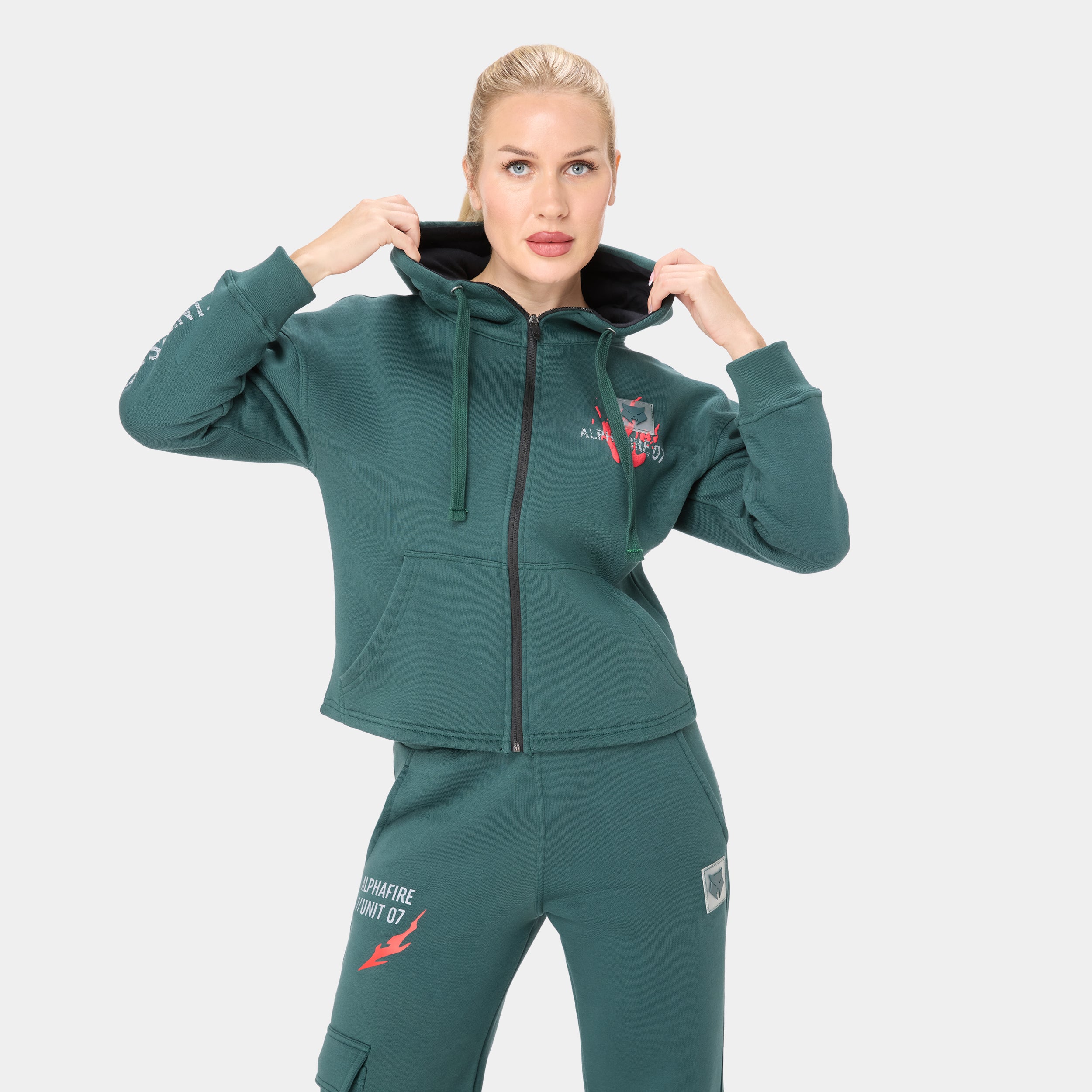 ALPHAFIRE CROP HOODIE — IRON FOREST — Front close-up torso, model holding hood up, teal cropped zip hoodie with Alphafire