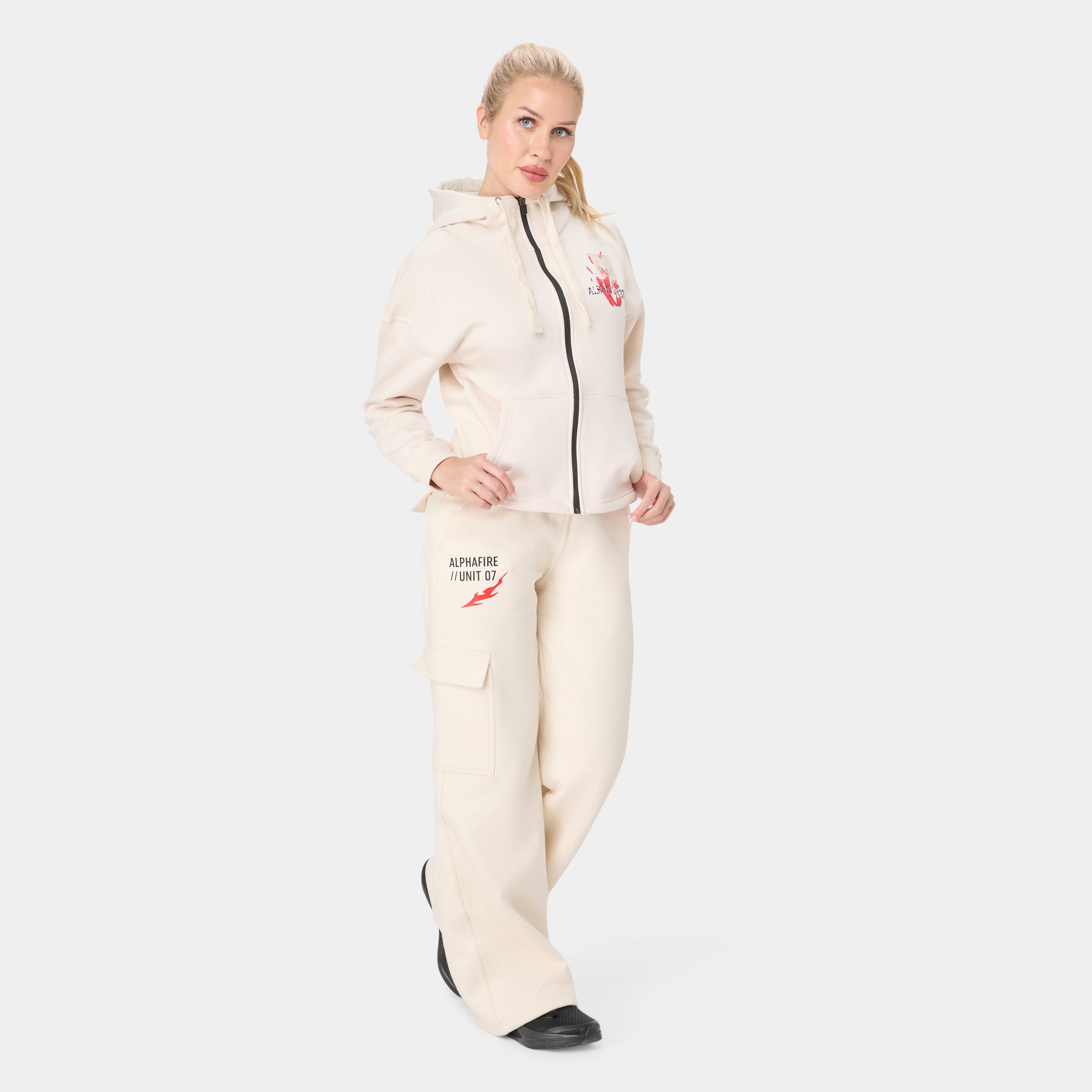 ALPHAFIRE CROP HOODIE — TACTICAL BEIGE — Full-body front ¾, cream tracksuit with Alphafire Unit 07 thigh graphic and light...