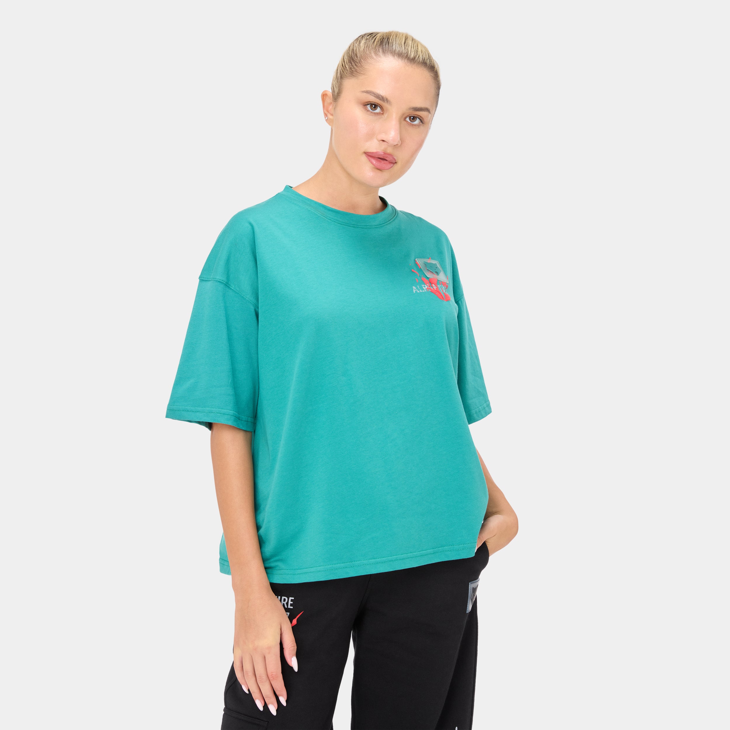 ALPHAFIRE OVERSIZED T-SHIRT — ROUGE GREEN — Front ¾ close-up, teal oversized tee with Alphafire chest graphic, hand in pocket