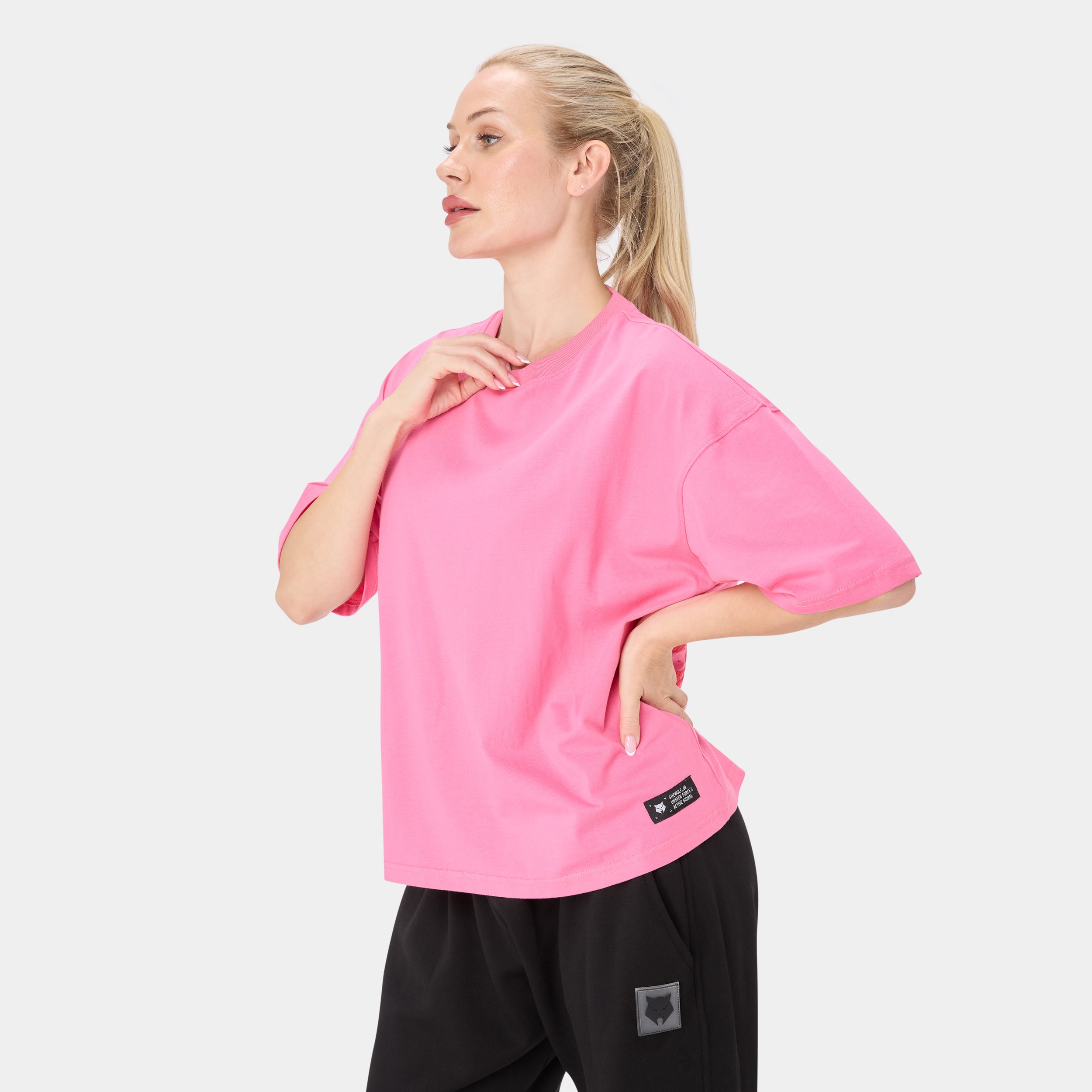 SHEWOLF_09 OVERSIZED TEE — ALPHA ROSE — Side/three-quarter view on female model, pink oversized cropped tee with small brand