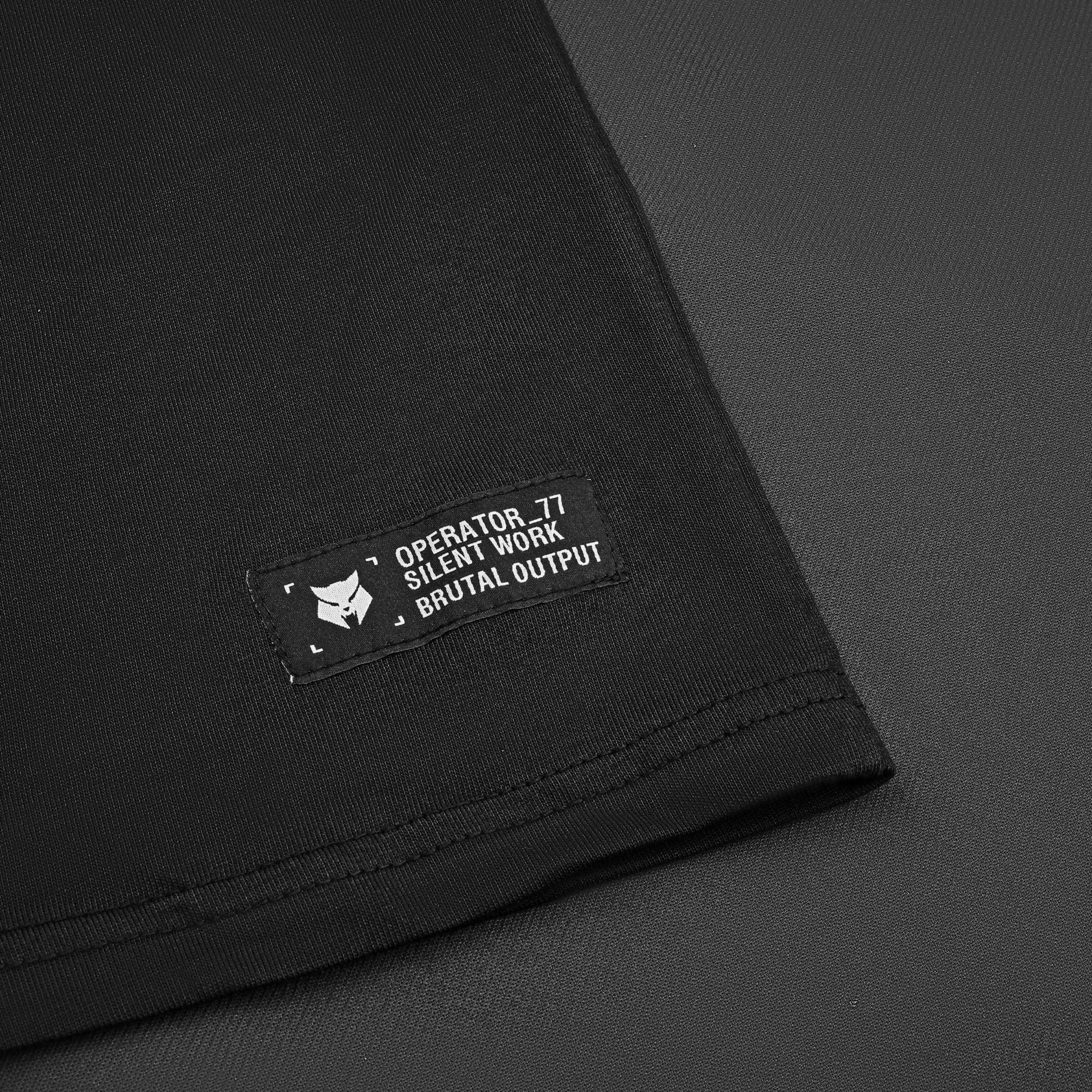 OPERATOR_77 OVERSIZED TEE — WAR BLACK — Flat-lay close-up, black tee Operator_77 Silent Work Brutal Output woven hem label w