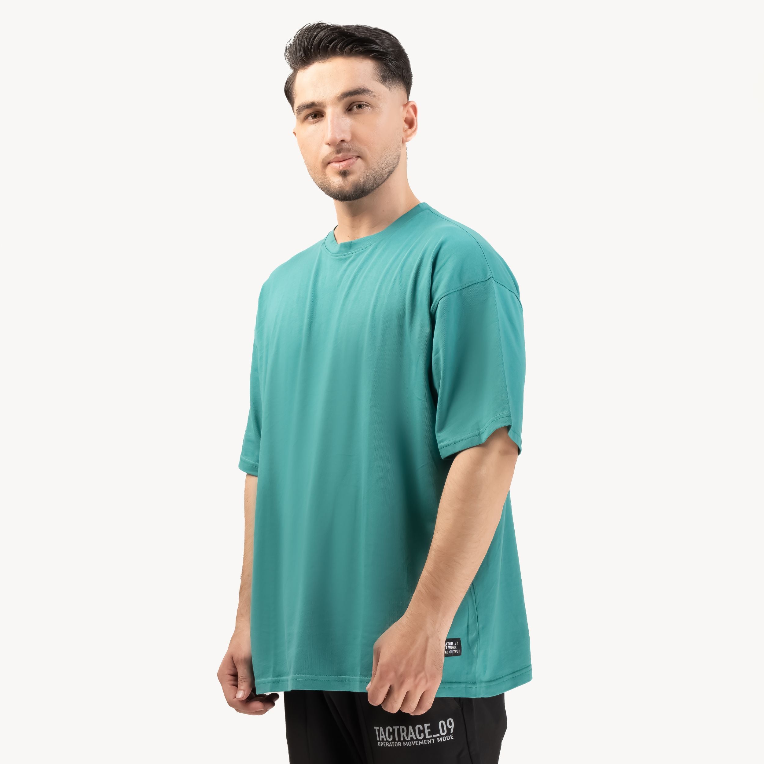 OPERATOR_77 OVERSIZED TEE — ROUGE GREEN — Three-quarter front view on male model, teal tee with minimal branding and small h